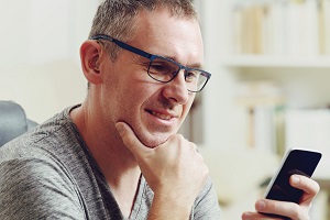 Image of man wearing hearing aid looking at smartphone.