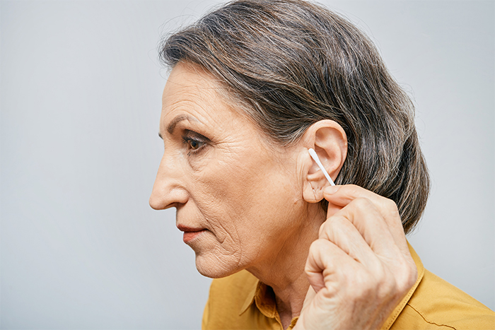 Mature woman cleans her ear from earwax with a cotton swab.