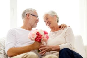 elderly couple sitting on a couch holding a bouquet of pink flowers